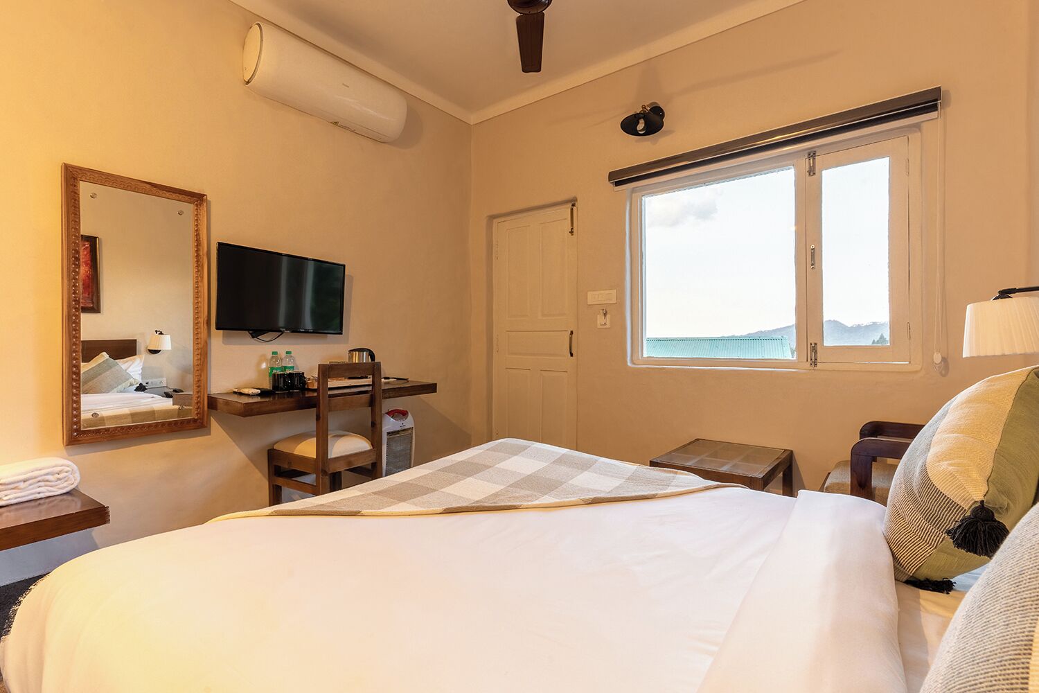 A hotel room with a bed, a desk, a chair, a television, a window, and a mirror.