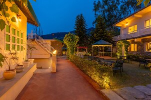 A well-lit outdoor area with a pathway leading to a building entrance, surrounded by potted plants and outdoor seating.