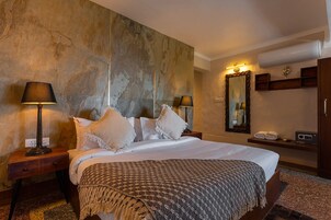 Habitación de hotel con una cama grande, dos lámparas de noche, un espejo, un estante con toallas y una pared con textura.