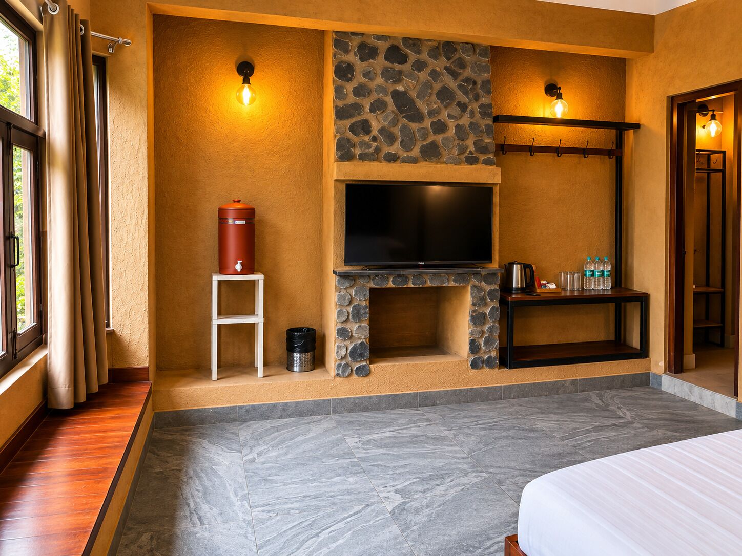 Una camera d'albergo con un camino in pietra, una TV a schermo piatto, un tavolino con bottiglie d'acqua e un letto.
