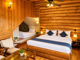 A log cabin-style room with a bed, a chair, a table with a candle, and a ceiling fan.
