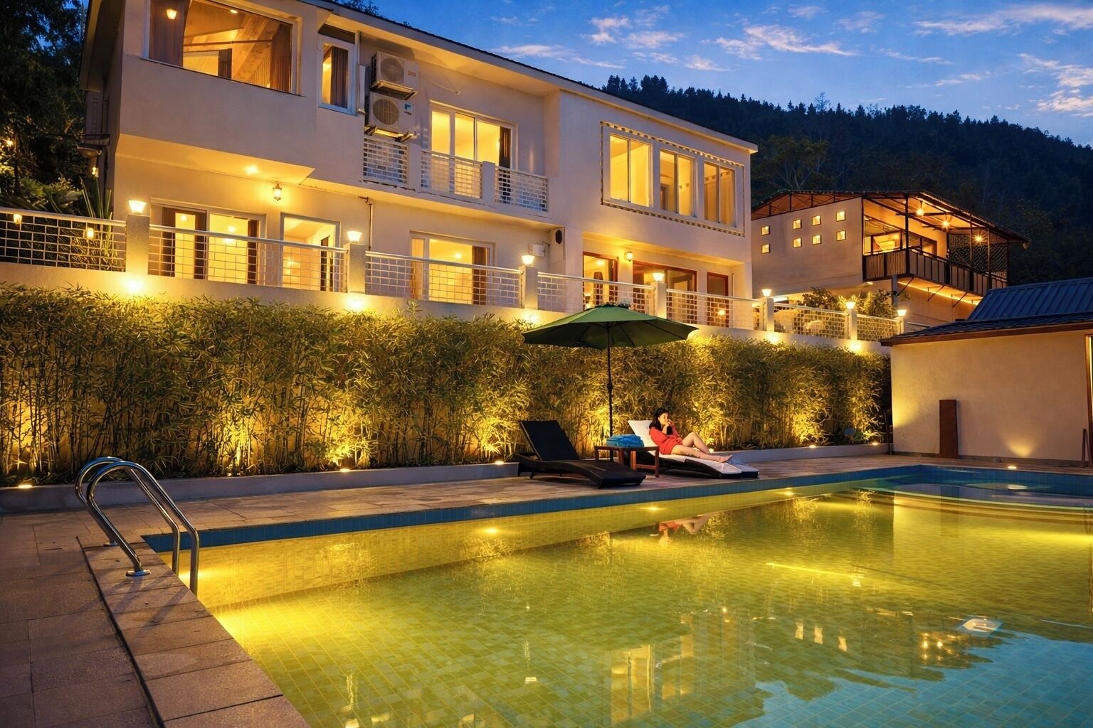 A modern two-story building with a swimming pool, a covered seating area, and a well-lit exterior.