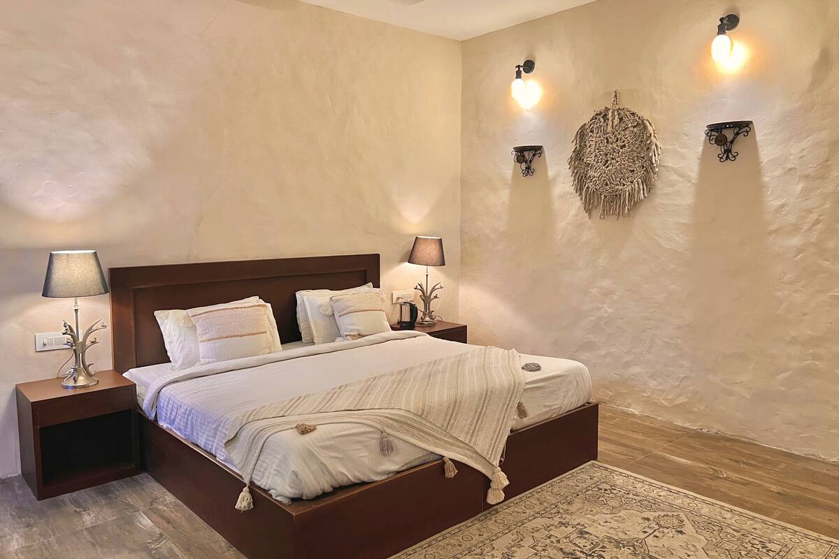 A bedroom with a wooden bed, two bedside tables with lamps, a wall-mounted light fixture, and a decorative wall hanging.
