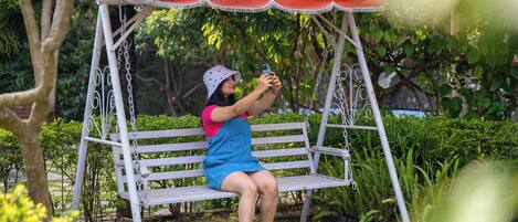 A person sitting on a white swing with a red canopy, surrounded by greenery.
