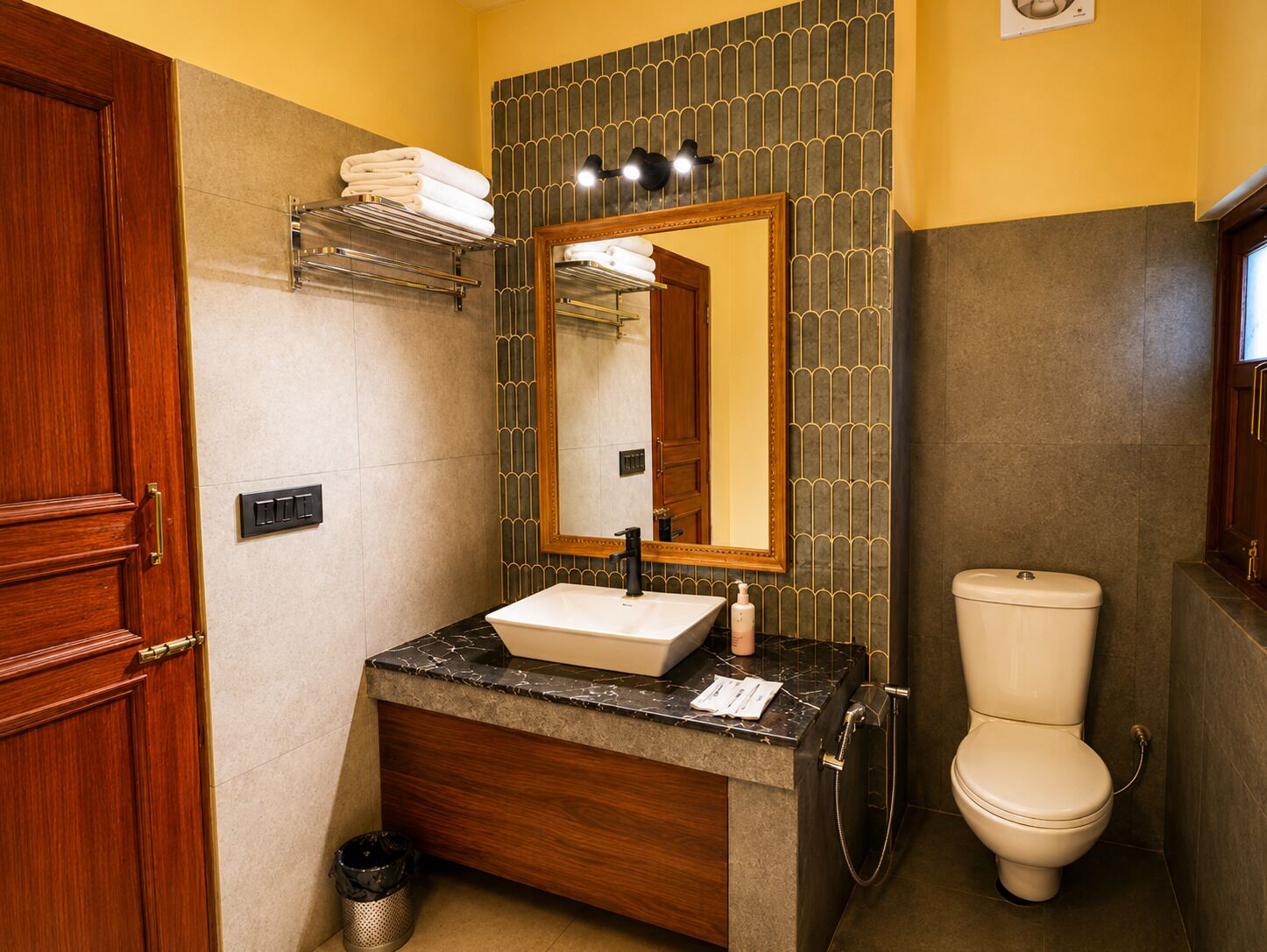 Un baño con lavamanos de mármol, inodoro, toallero y espejo.