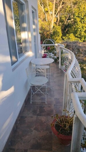 A small outdoor patio with a white metal table and chairs, a potted plant, and a white railing. - MAATI Resort by The Lake Hill (Nainital)
