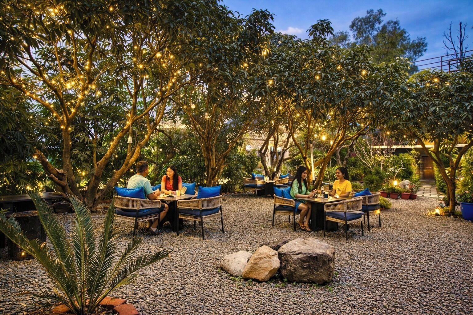 Un espace de restauration en plein air, avec des tables et des chaises, entouré d’arbres et illuminé par des guirlandes lumineuses.