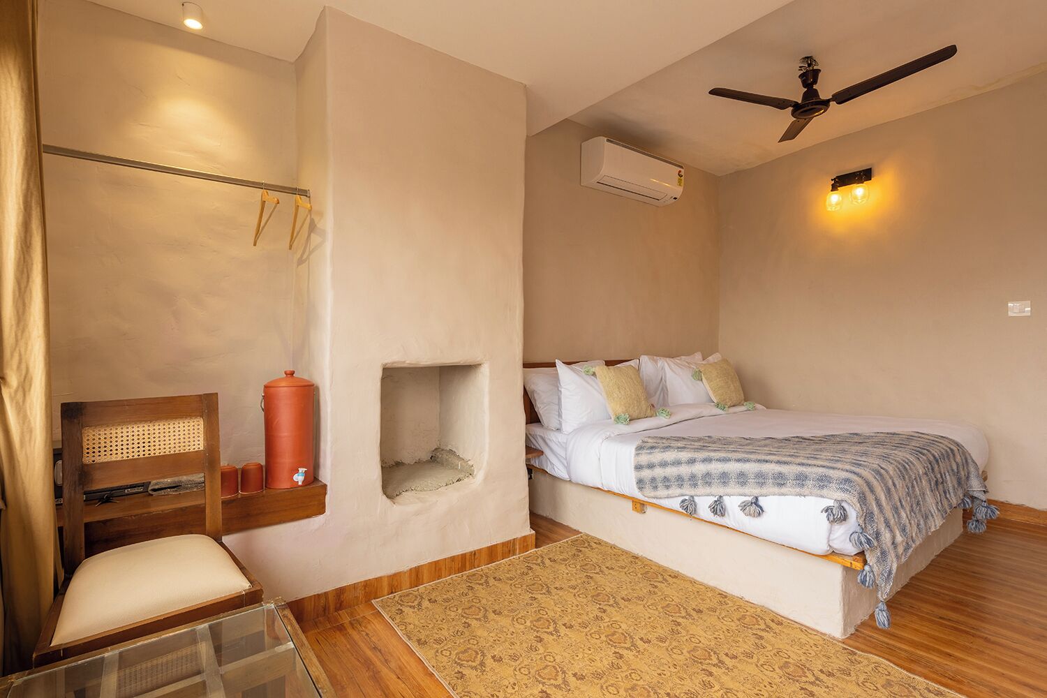 A bedroom with a bed, a chair, a small table, an air conditioning unit, and a ceiling fan.