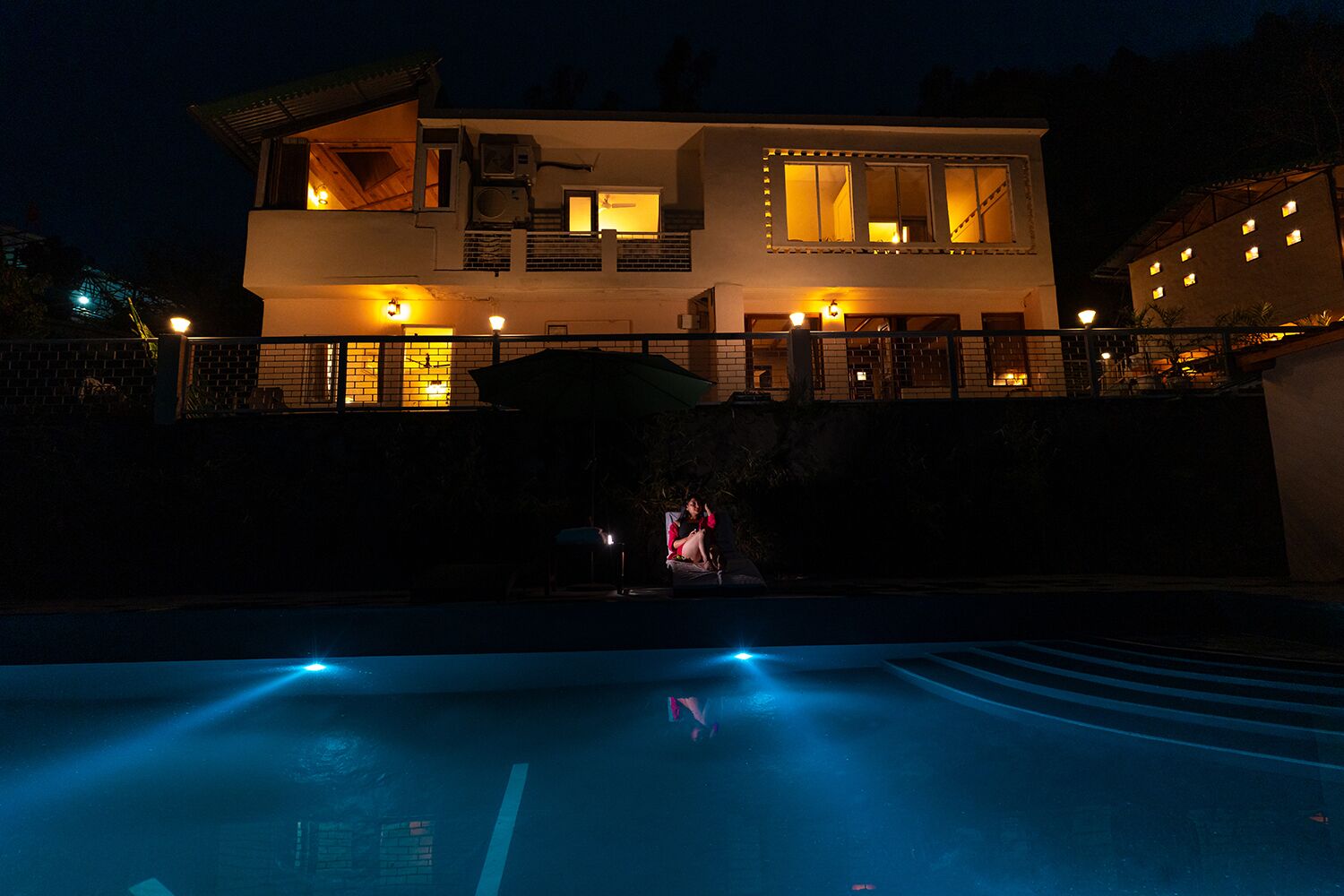 A modern house with a swimming pool at night, illuminated by warm lights.