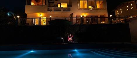 A modern house with a swimming pool at night, illuminated by warm lights.