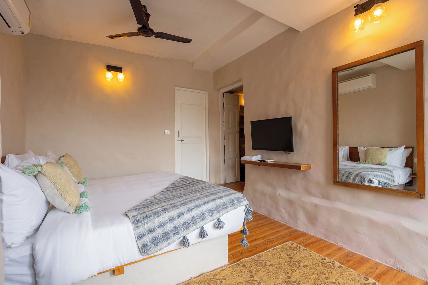 A bedroom with a bed, a television, a ceiling fan, a mirror, and a door.