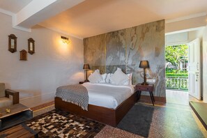 A bedroom with a large bed, two bedside lamps, a wooden nightstand, a patterned rug, and a view of greenery through an open door. - MAATI Resort by The Lake Hill (Nainital)