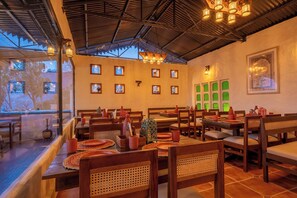 A restaurant with wooden tables and chairs, framed pictures on the walls, and a view of trees through the windows. - MAATI Resort by The Lake Hill (Nainital)