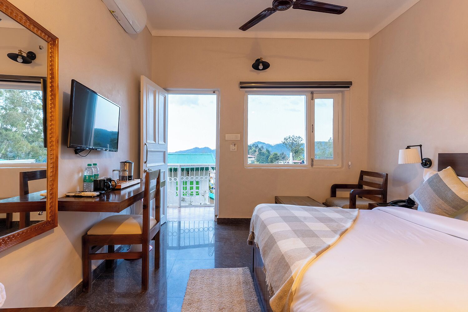 A hotel room with a bed, a desk with a chair, a television, and a balcony with a view of the mountains.