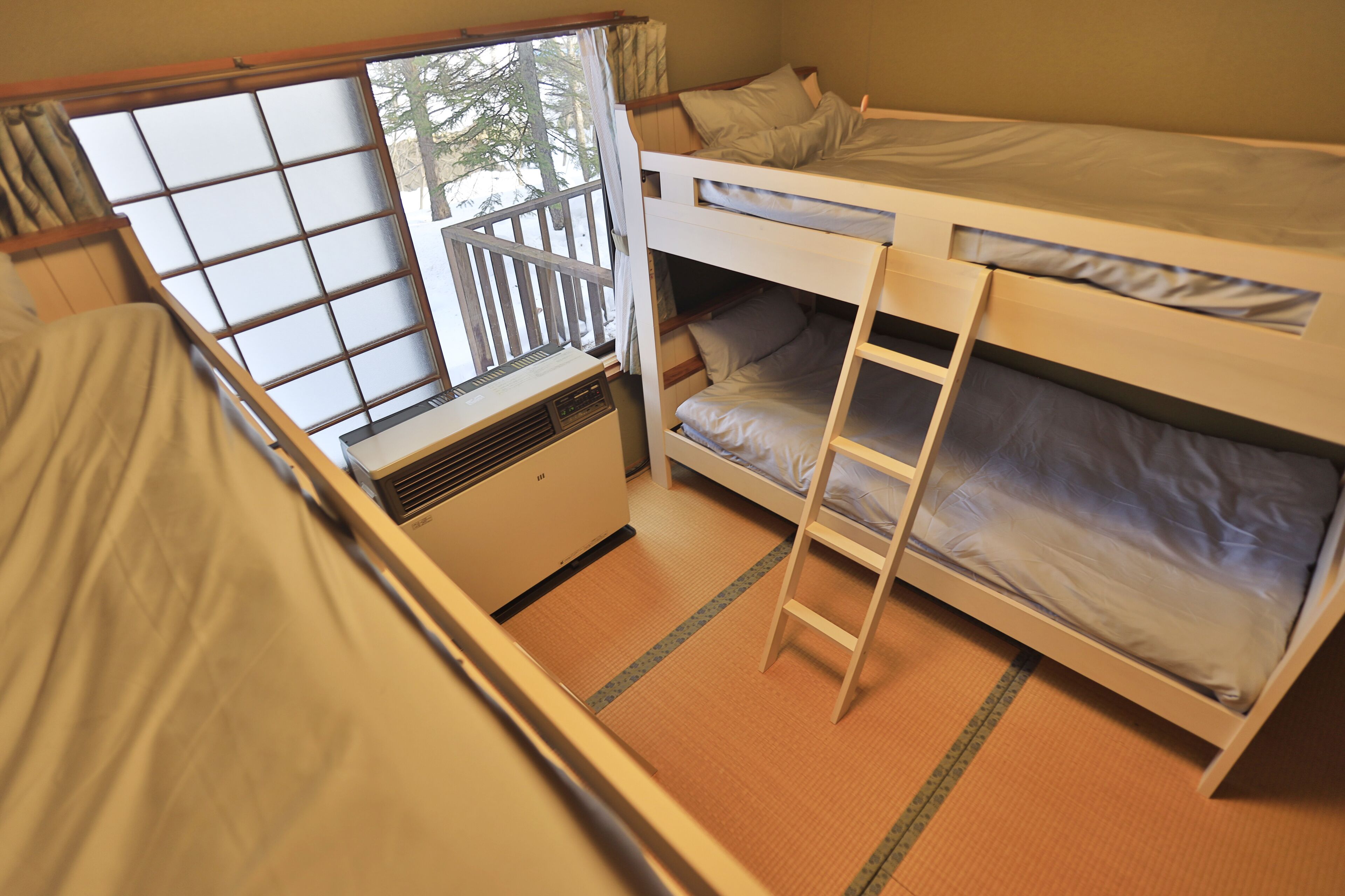 A dormitory room with bunk beds, a window with a view of trees, and a heater.