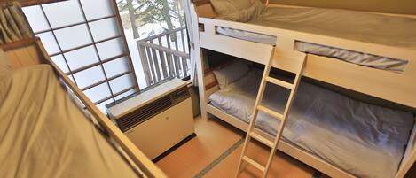 A dormitory room with bunk beds, a window with a view of trees, and a heater.