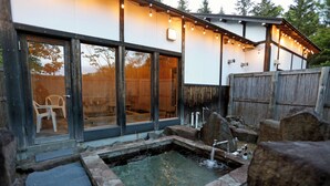 Ein Wellnessbereich mit Whirlpool, Holzterrasse und einem Gebäude mit großen Fenstern und Lichterketten.