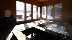 Ein Wellnessbereich mit Steinböden, einer Whirlwanne, großen Fenstern und Holzvertäfelung.