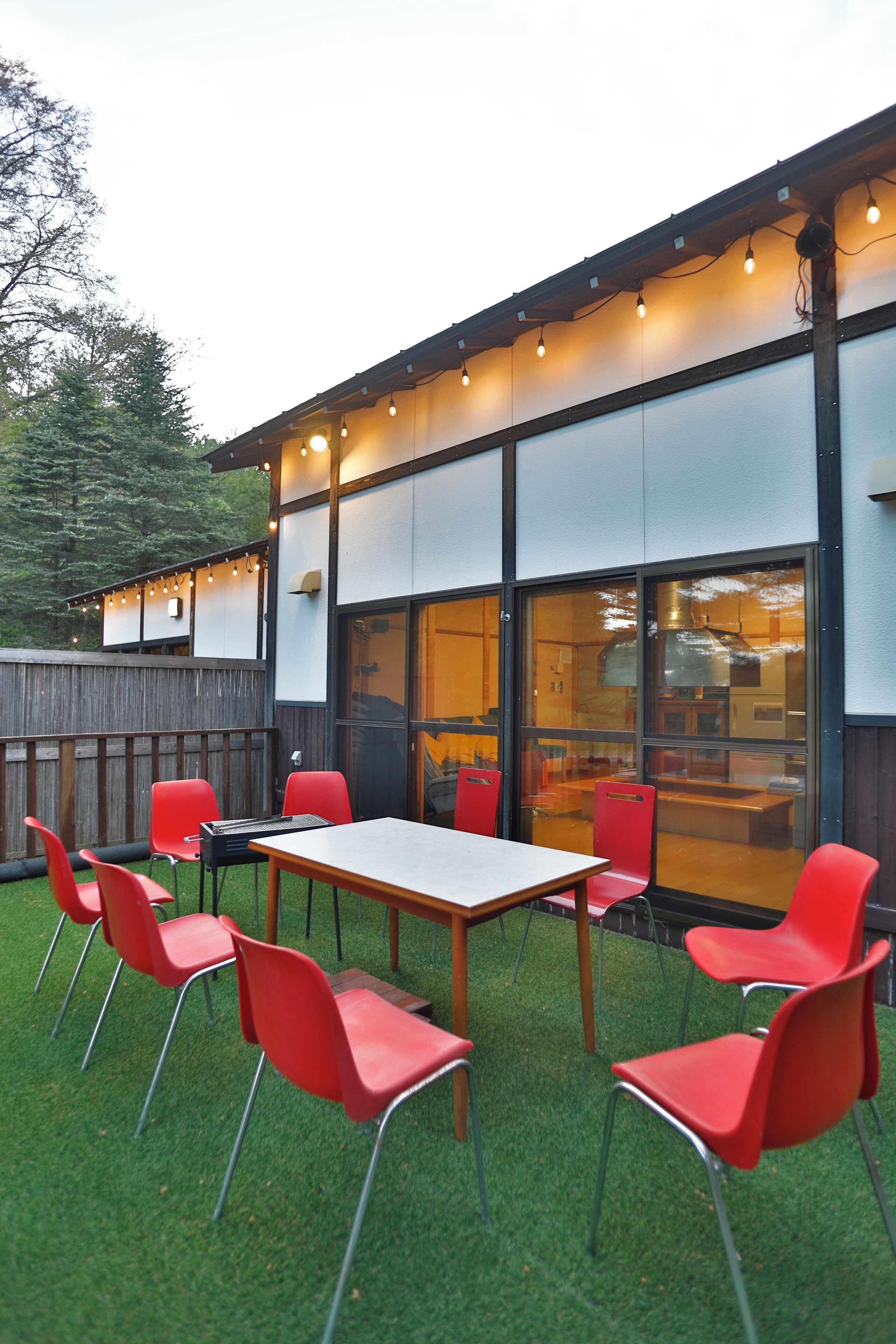 Une terrasse extérieure avec une table en bois et des chaises rouges, une clôture en bois et des guirlandes lumineuses.