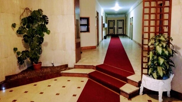 A hotel lobby with a red carpet, marble flooring, potted plants, and a wooden screen. - Das Karma - Bruzzi (Genova)