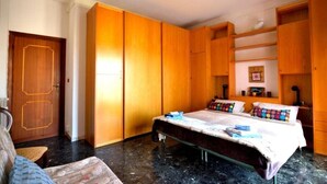 A bedroom with a bed, wooden wardrobe, and a small seating area. - Das Karma - Bruzzi (Genova)