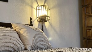 A bedroom with a bed, a wall-mounted light fixture, and a wooden door. - Casa Rural con Terraza y Barbacoa en Pleno Parque Natural (El Ojuelo)