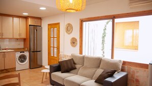 A compact kitchen with a washing machine, a refrigerator, and a dining area with a sofa and table. - Casa Rural con Terraza y Barbacoa en Pleno Parque Natural (El Ojuelo)