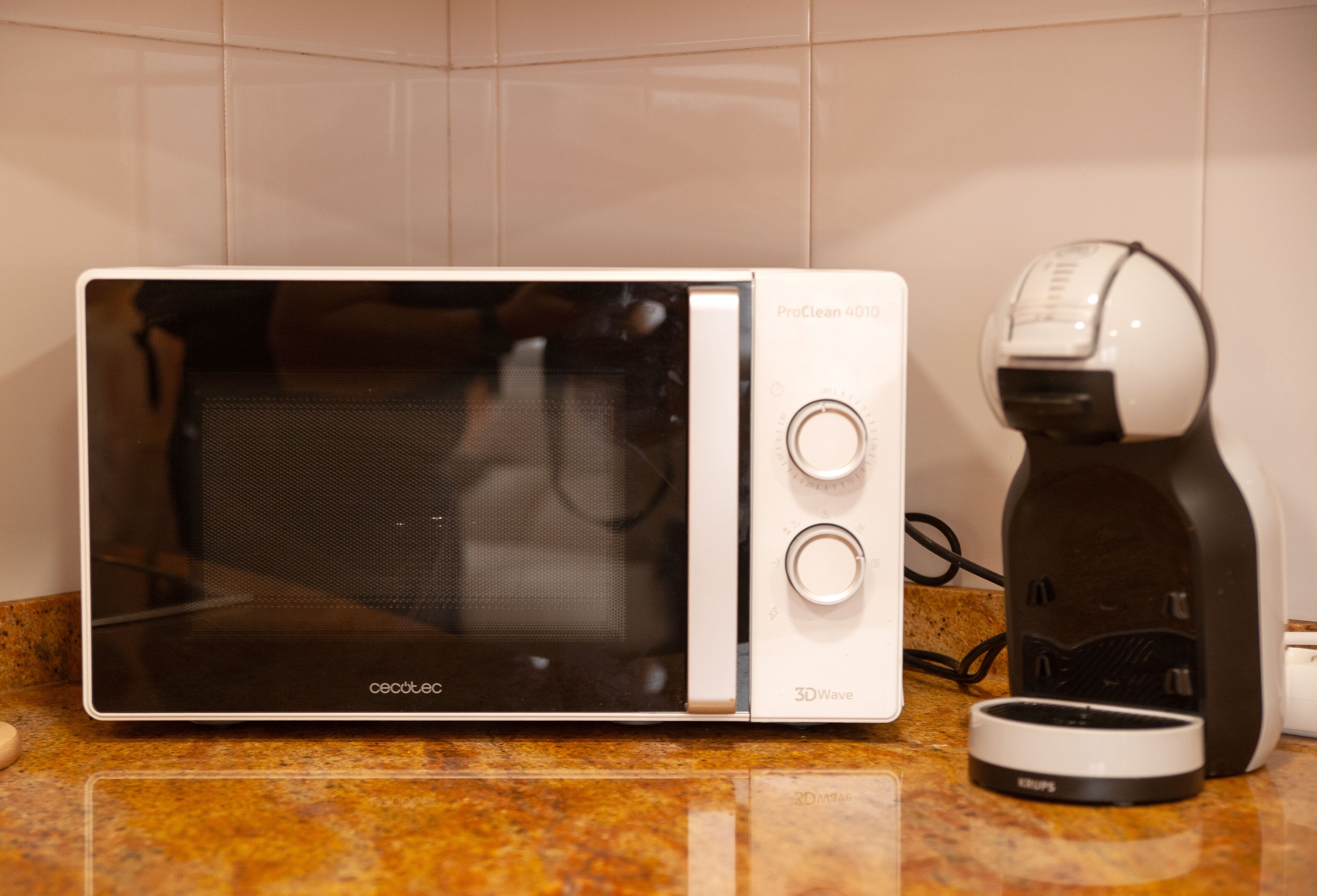 A microwave oven with a 3D wave feature and a coffee maker on a kitchen countertop.