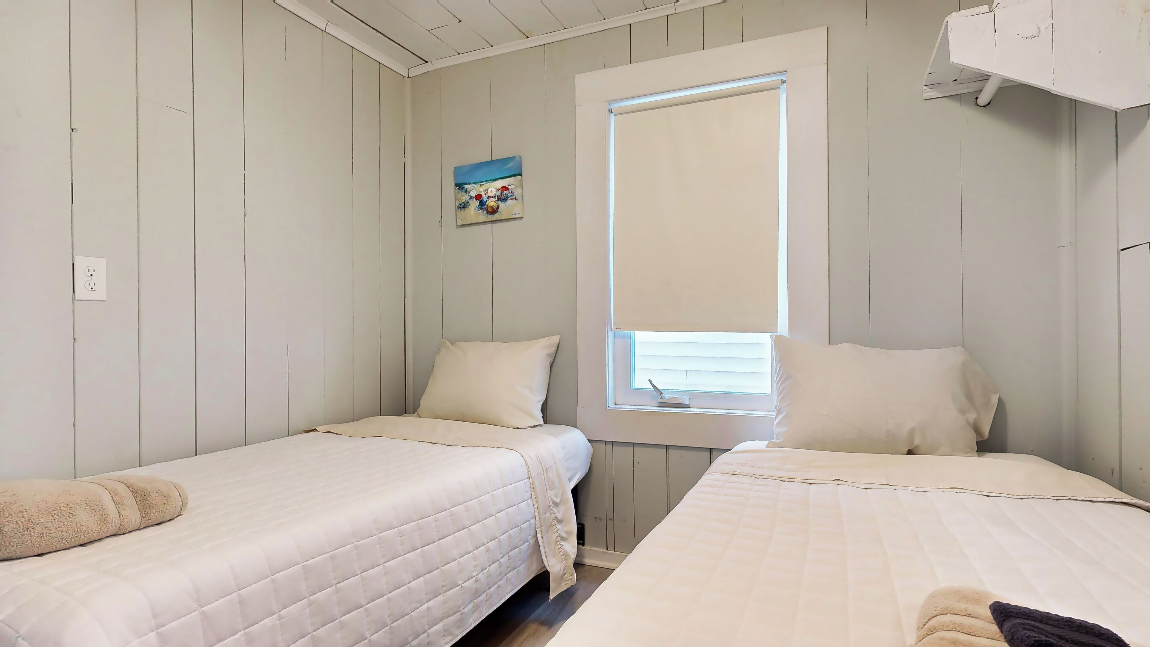 Een kamer met twee bedden, een raam met zonwering, een schilderij aan de muur en een stopcontact.