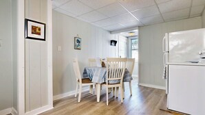 Une cuisine avec une table et des chaises en bois, un réfrigérateur blanc et une fenêtre laissant entrer la lumière naturelle.