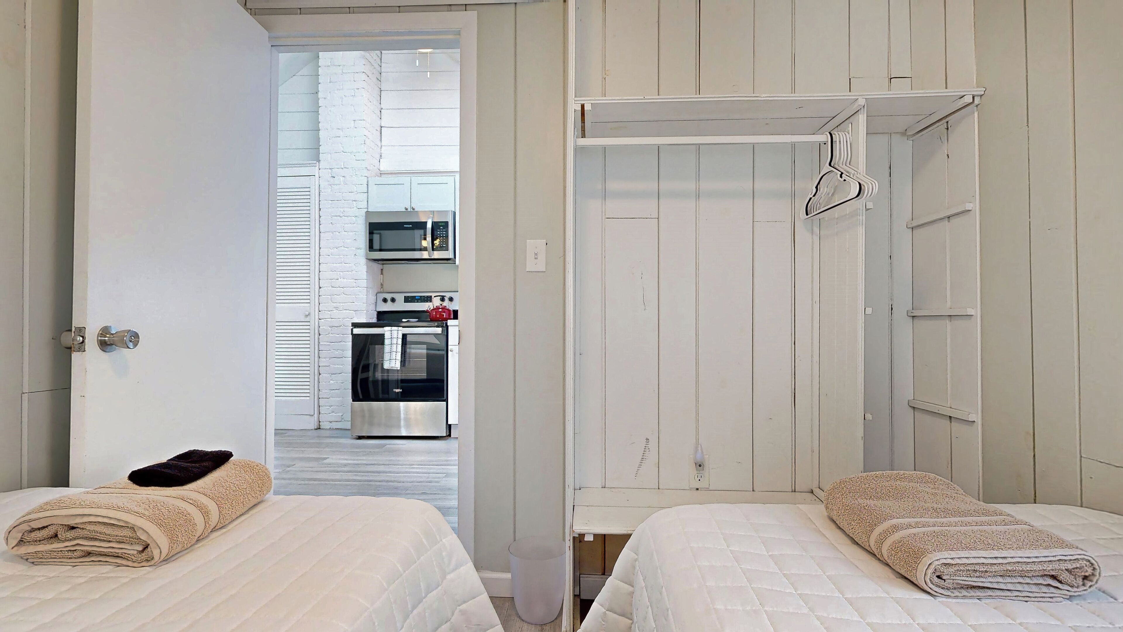 Habitación de hotel con dos camas, un armario y una kitchenette al fondo.