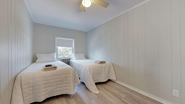 A bedroom with two beds, a ceiling fan, a window, and a wooden floor.