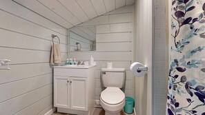 A bathroom with white wooden walls, a white sink with toiletries, a toilet, and a mirror. - Salt Life #2 by Bayley Vacation Rentals (Old Orchard Beach)