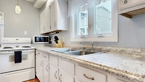 A modern kitchen with white cabinets, a granite countertop, a built-in microwave, and a stainless steel sink. - Sand Life #1 by Bayley Vacation Rentals (Old Orchard Beach)