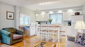 A modern kitchen with white cabinets, a dining table, and chairs. There is a sofa and a coffee table in the living area. - Sand Life #1 by Bayley Vacation Rentals (Old Orchard Beach)
