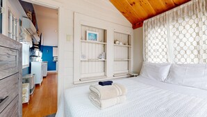 A bedroom with a bed, a window with patterned curtains, and a view of the kitchen. - Sand Life #2 by Bayley Vacation Rentals (Old Orchard Beach)