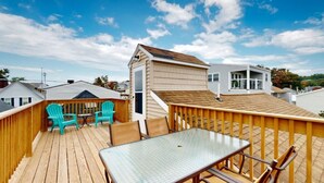 A wooden deck with a table and chairs, a small covered area with chairs, and a building in the background. - Sand Life #2 by Bayley Vacation Rentals (Old Orchard Beach)