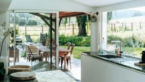 A modern kitchen with a large island, a dining area with outdoor seating, and a view of the garden. - Le Domaine de la Source (Pennedepie)