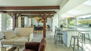 A spacious living area with a sofa, a dining table with chairs, and a kitchen area with a bar. - Le Domaine de la Source (Pennedepie)
