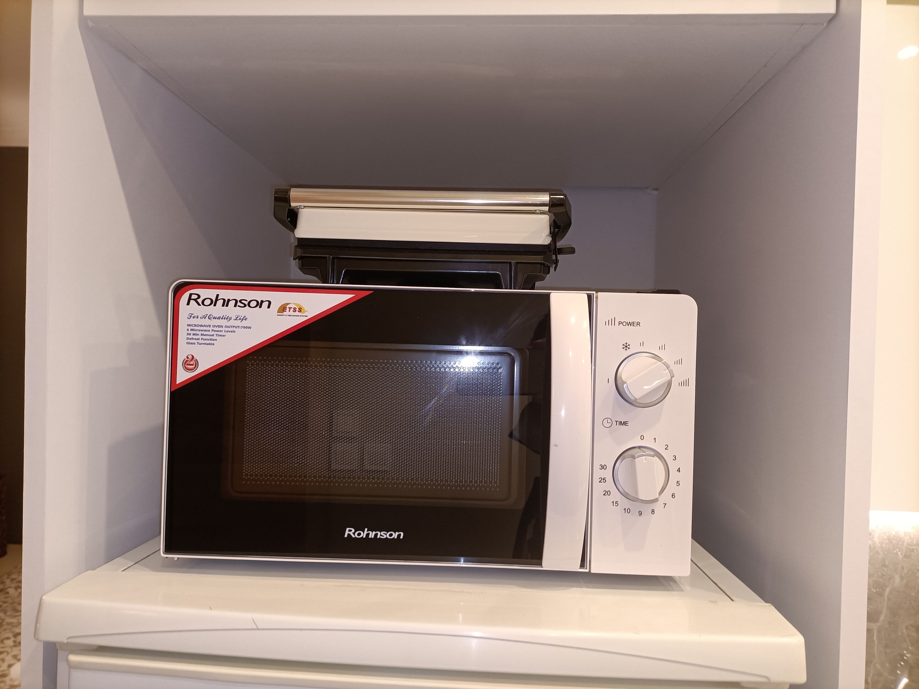 Un four à micro-ondes doté d’un écran numérique et d’un panneau de commande, installé à l’intérieur d’un meuble blanc.