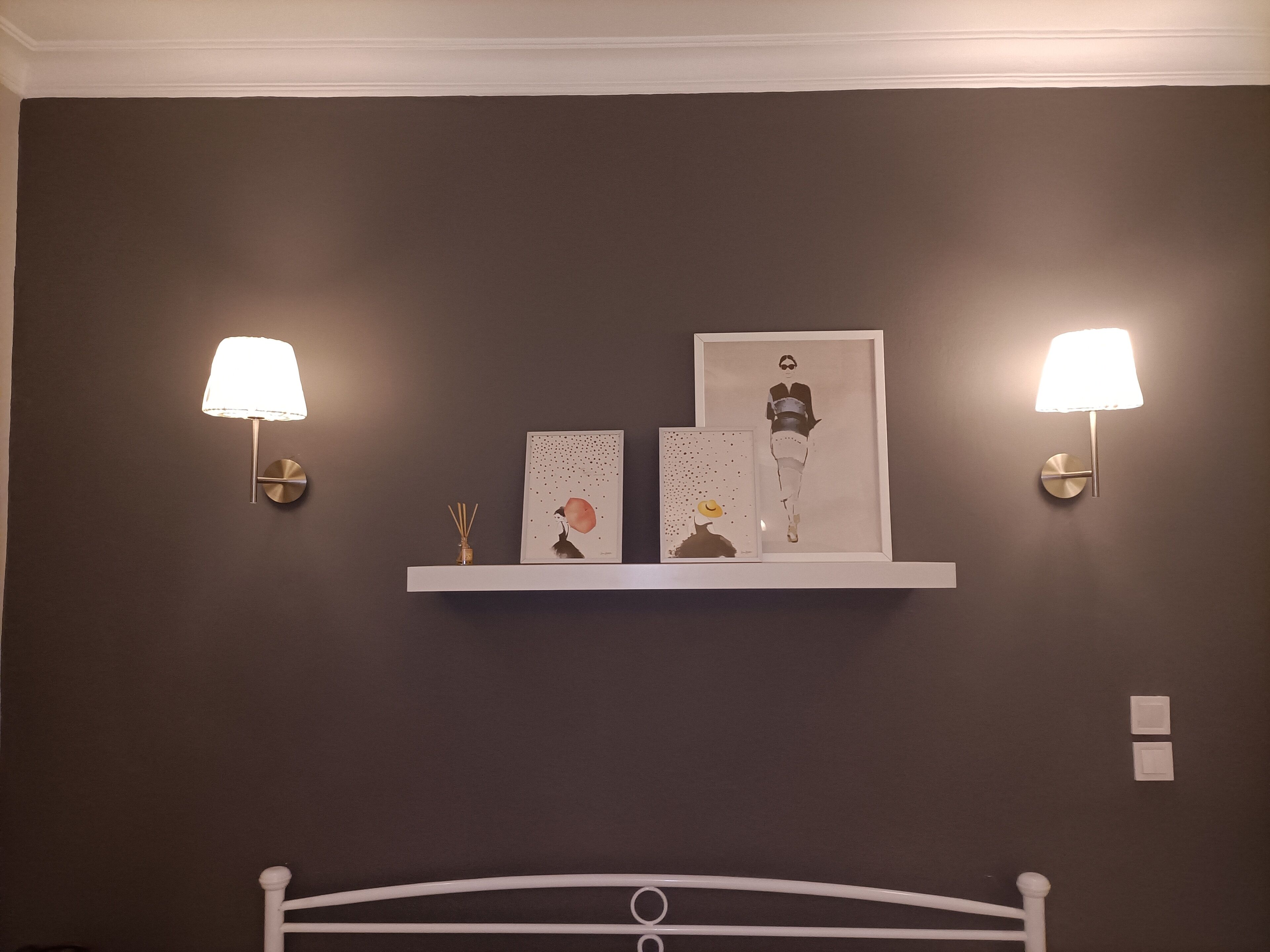A bedroom with a bed, two wall-mounted lamps, and a shelf with artwork and a vase.