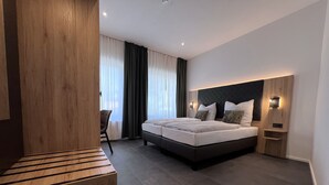 A modern hotel room with a large bed, a wooden bench, a desk, and a chair. - Haus Kuckenberg (Burscheid)