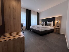 Quarto de hotel moderno com uma cama grande, um banco de madeira, uma escrivaninha e uma cadeira.