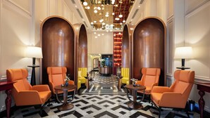 Eine Lobby mit Schachbrettfußboden, orangefarbenen Sesseln, einem zentralen Couchtisch und einer Chandelüster.