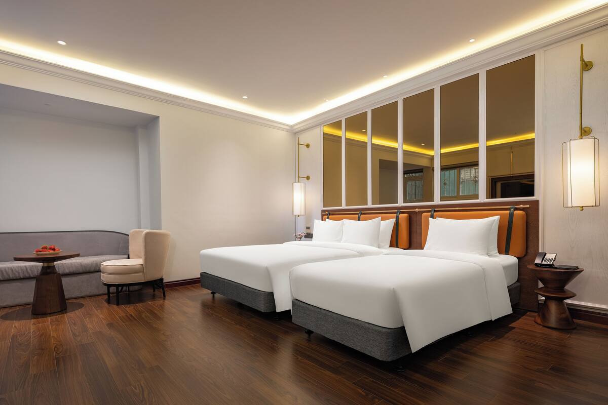 A hotel room with two beds, a sofa, a small table, and a mirror.
