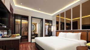 Ein Hotelzimmer mit einem großen Bett, einem Schreibtisch mit Kaffeemaschine, einem Spiegel und Blick auf die Stadt durch große Fenster.