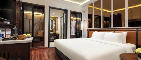 A hotel room with a large bed, a desk with a coffee maker, a mirror, and a view of the city through large windows.