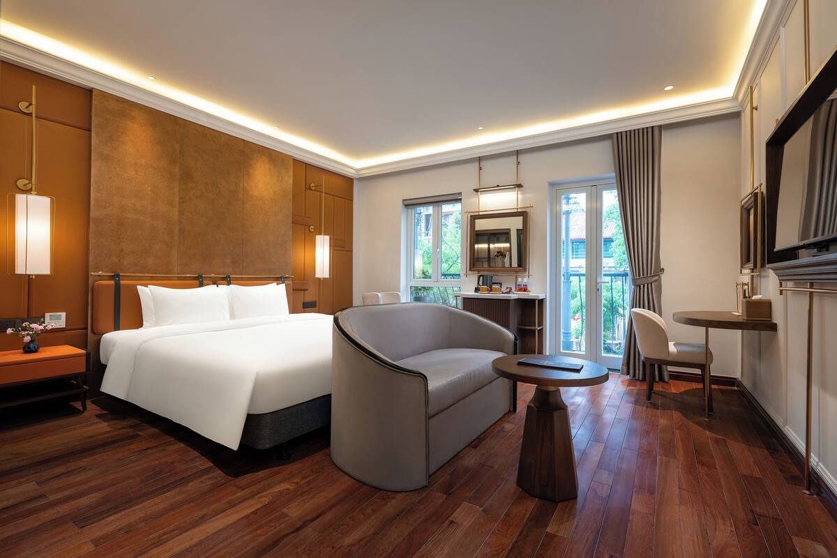 A hotel room with a large bed, a sofa, a small table, and a TV.