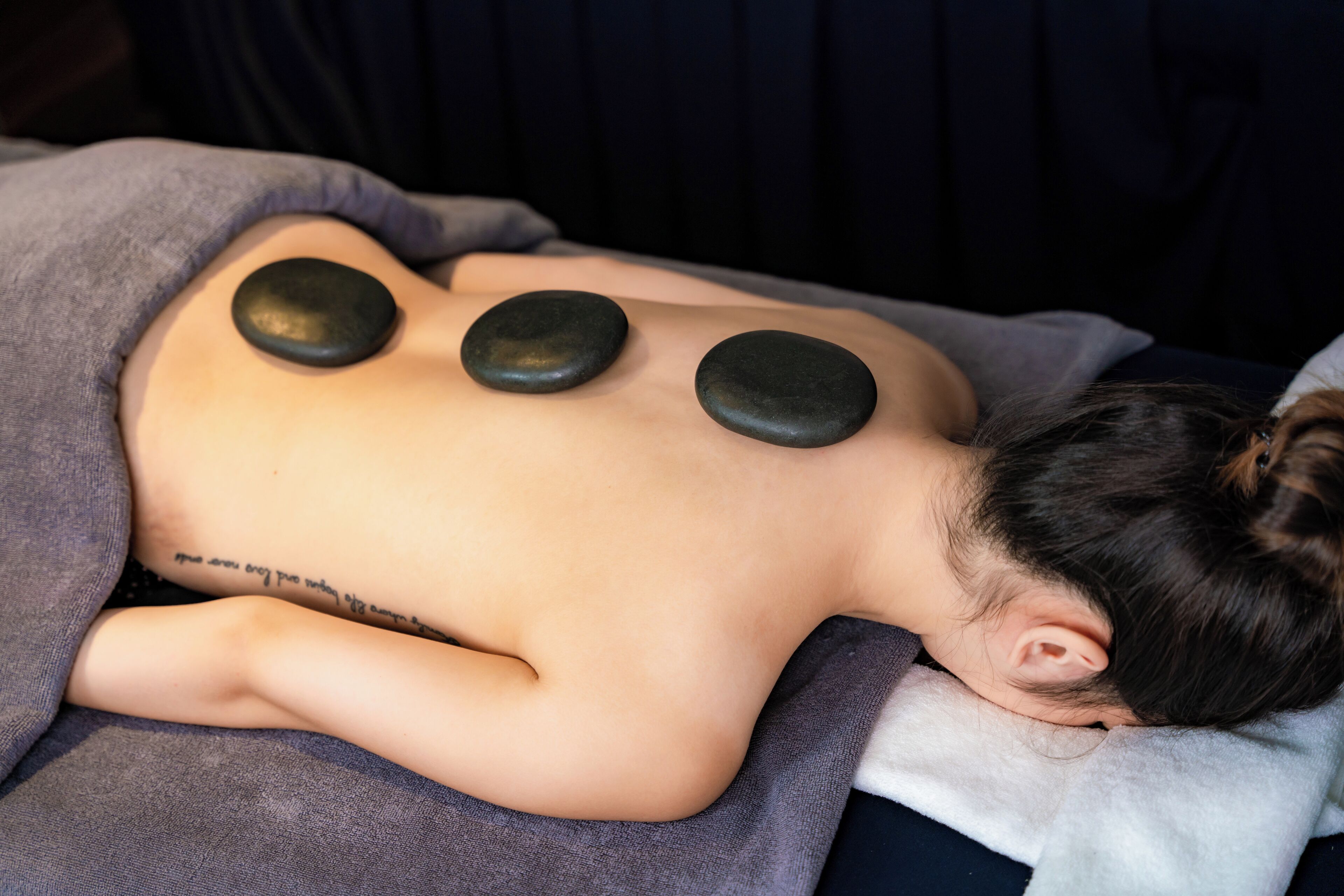 A person receiving a back massage with three heated stones placed on their back.