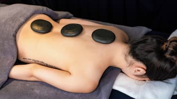 A person receiving a back massage with three heated stones placed on their back.